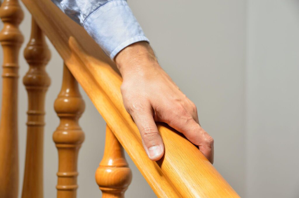 Close-up of a hand gripping a wooden staircase handrail for support.